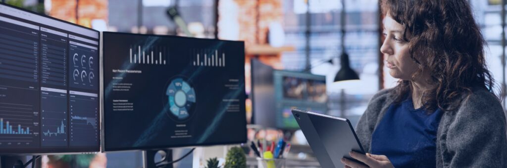 Kanerika vs Sigmoid blog banner showing a data professional reviewing analytics dashboards on office monitors.