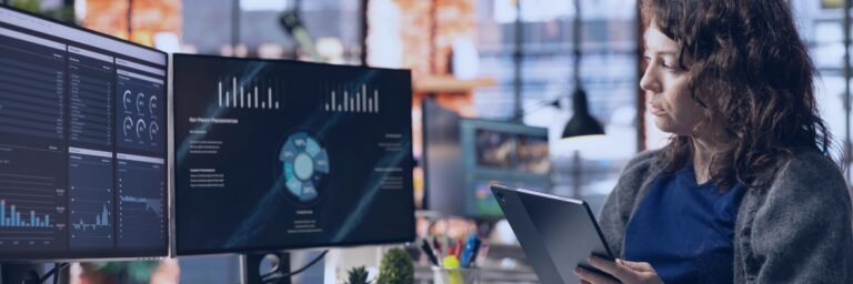 Kanerika vs Sigmoid blog banner showing a data professional reviewing analytics dashboards on office monitors.