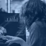 Analyst pointing at an AI performance metrics dashboard with charts on a monitor, Kanerika blog banner