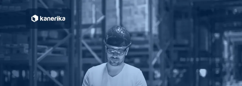Warehouse manager in a hard hat reviewing a tablet between storage racks, illustrating supply chain analytics tools