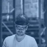 Warehouse manager in a hard hat reviewing a tablet between storage racks, illustrating supply chain analytics tools