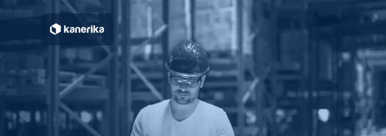 Warehouse manager in a hard hat reviewing a tablet between storage racks, illustrating supply chain analytics tools