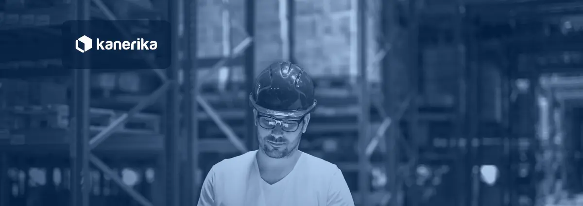 Warehouse manager in a hard hat reviewing a tablet between storage racks, illustrating supply chain analytics tools