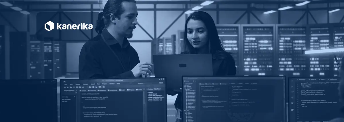 Two data engineers reviewing code on a laptop in a server room while planning a Unity Catalog migration on Databricks