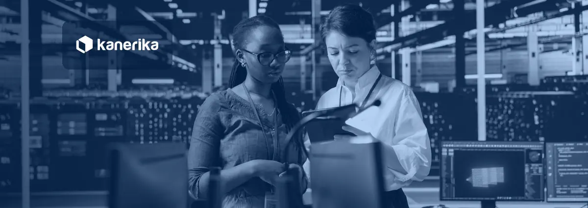 Two data engineers reviewing migration data on a tablet in a server room with monitors in the background