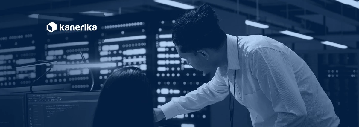 Two data center engineers reviewing code on a monitor beside server racks, Kanerika banner for data conversion vs data migration