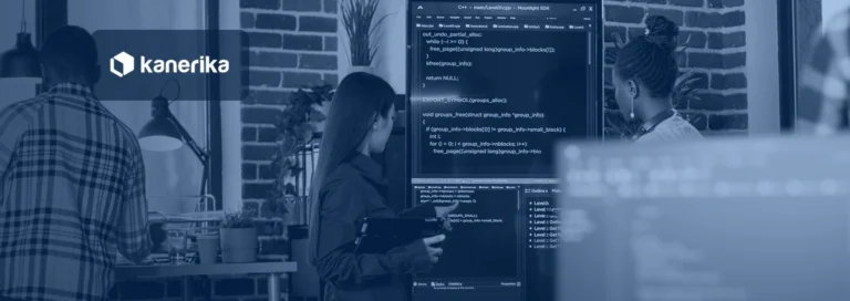 Engineer with a tablet explaining code on a wall screen to a team, representing explainable AI, shown in a navy blue tint with the Kanerika logo