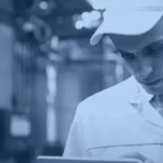 Technologist in a white coat using a tablet on a food factory floor, banner image for the Kanerika QAD Fabric mirroring guide