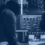 Data engineers reviewing a data flow on screens in a server room, illustrating Snowflake data sharing between accounts