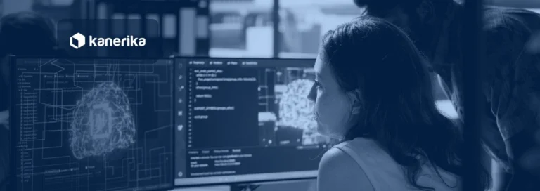 Data scientists reviewing a machine learning model on dual monitors, representing machine learning versus AI, shown in a navy blue tint with the Kanerika logo