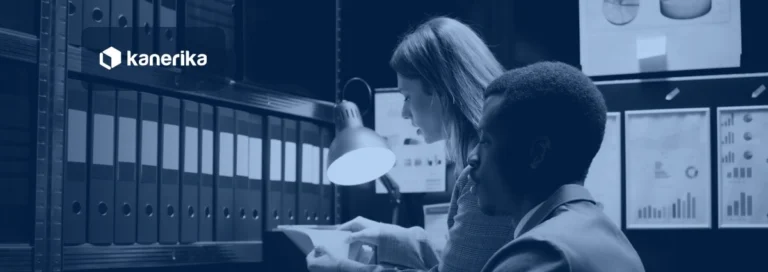 Colleagues reviewing documents in a records archive, representing Microsoft Fabric governance and compliance, shown in a navy blue tint with the Kanerika logo