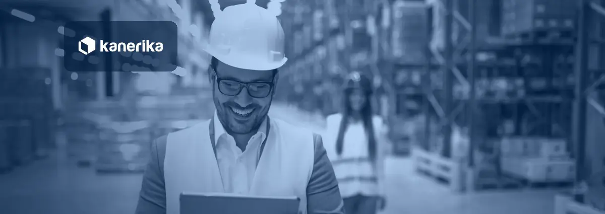 Smiling warehouse manager in a hard hat and safety vest reading a tablet in a distribution centre, in a navy-blue tint with the Kanerika logo, for a post on supply chain automation